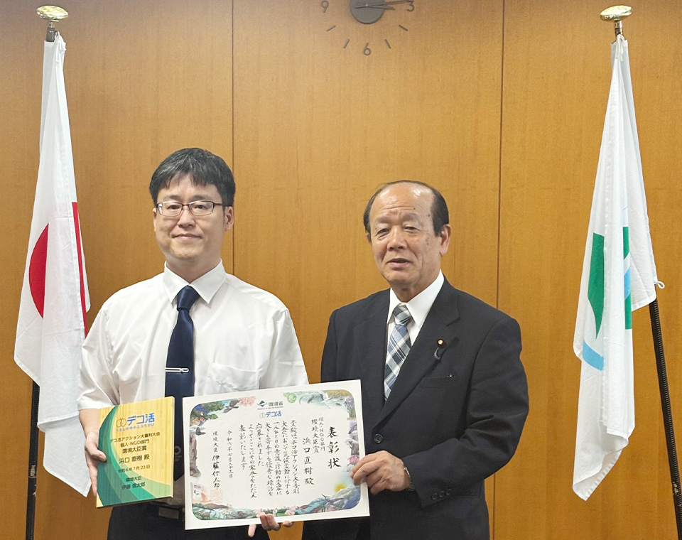個人・NGO部門受賞　神奈川県横須賀市在住の方と八木環境副大臣。表彰状と表彰楯を手にしています。